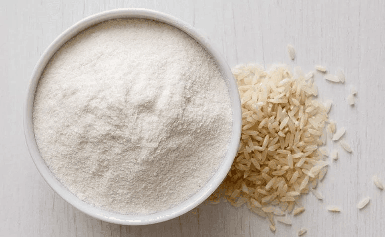 Farinha de arroz Granomax em tigela, ao lado de grãos de arroz